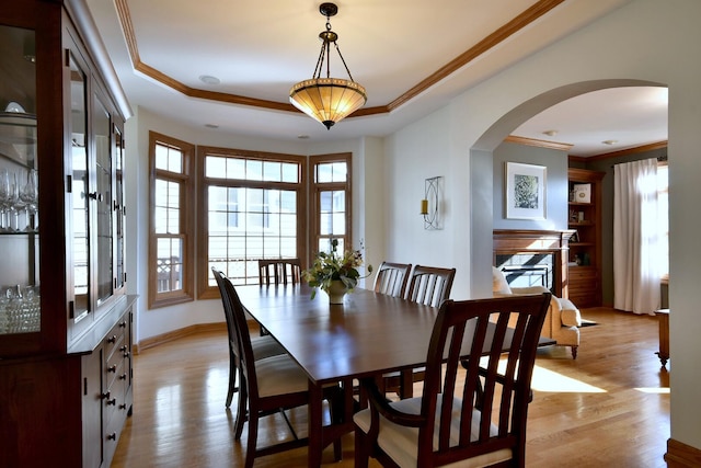 dining room featuring a tray ceiling, light wood-style flooring, arched walkways, and crown molding