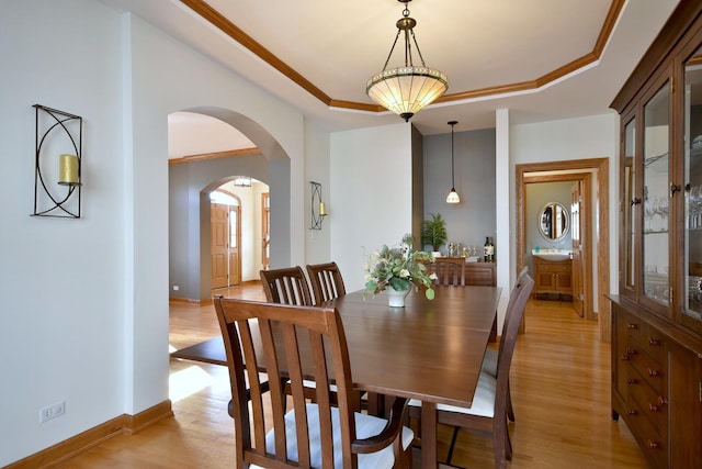 dining room featuring arched walkways, a raised ceiling, light wood-style flooring, and baseboards