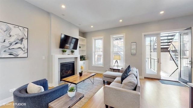 living area featuring light wood-type flooring, recessed lighting, stairs, and a glass covered fireplace