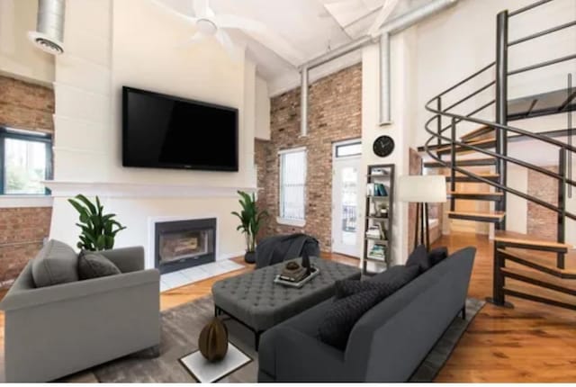 living area featuring a fireplace with flush hearth, a wealth of natural light, brick wall, and wood finished floors