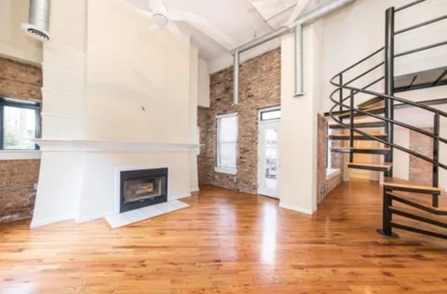 unfurnished living room with brick wall, a high ceiling, wood finished floors, and a wealth of natural light