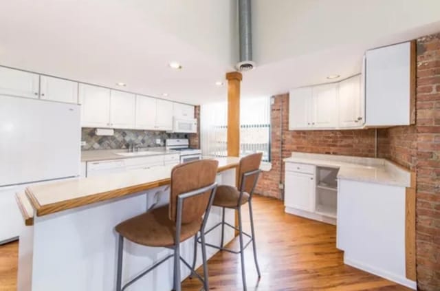 kitchen featuring light wood-style floors, white appliances, white cabinetry, and a breakfast bar area