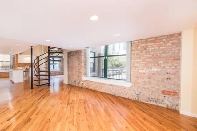 unfurnished living room featuring stairs, brick wall, and wood finished floors