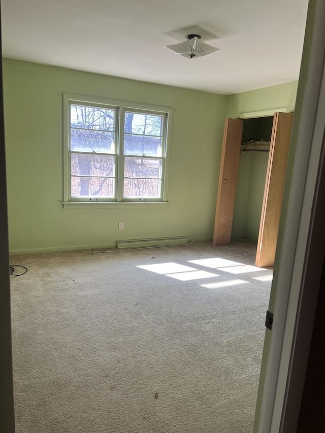 unfurnished bedroom with carpet floors, baseboard heating, and a closet