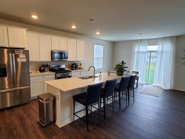 kitchen featuring a sink, a breakfast bar, appliances with stainless steel finishes, a center island with sink, and dark wood-style flooring
