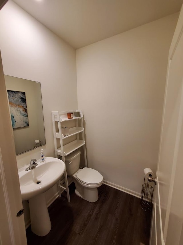 half bathroom with toilet, wood finished floors, and baseboards
