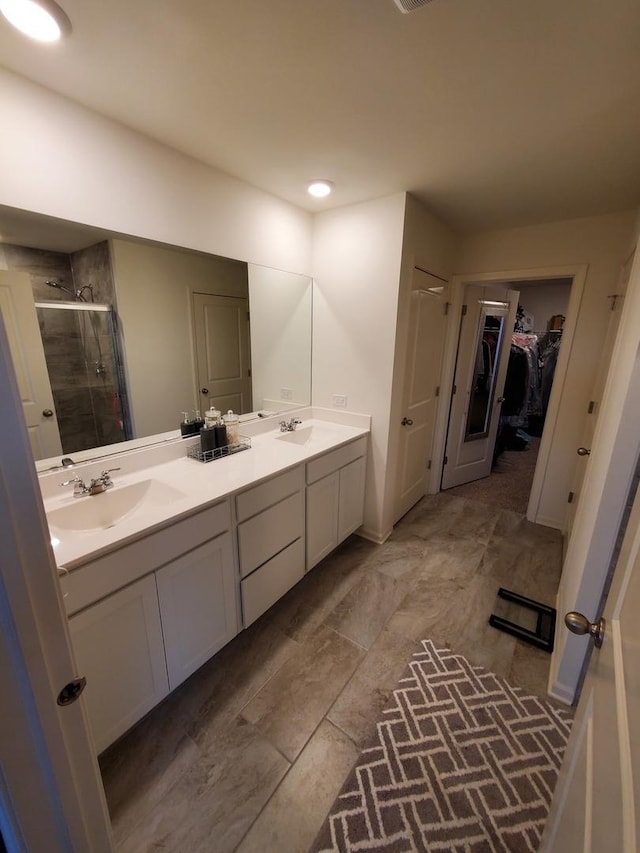 full bath featuring a stall shower, double vanity, a walk in closet, and a sink