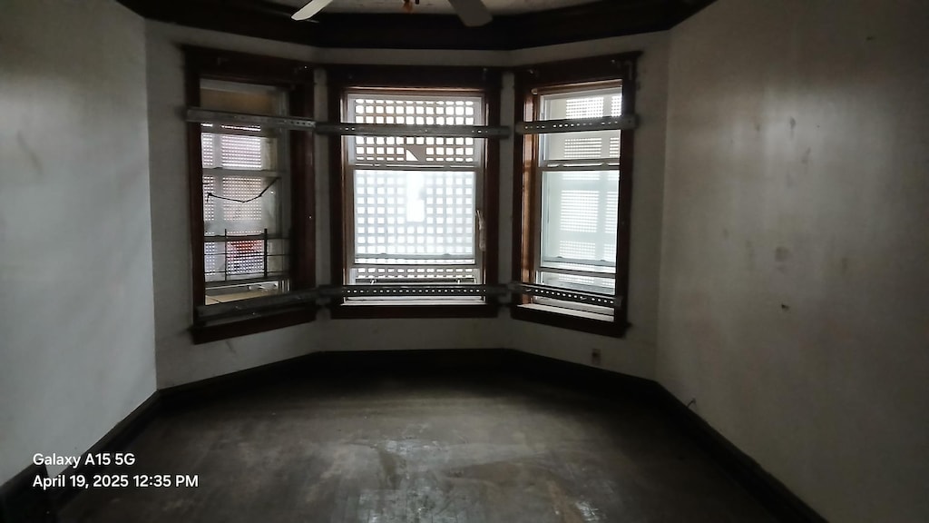 spare room featuring unfinished concrete floors, baseboards, and a ceiling fan