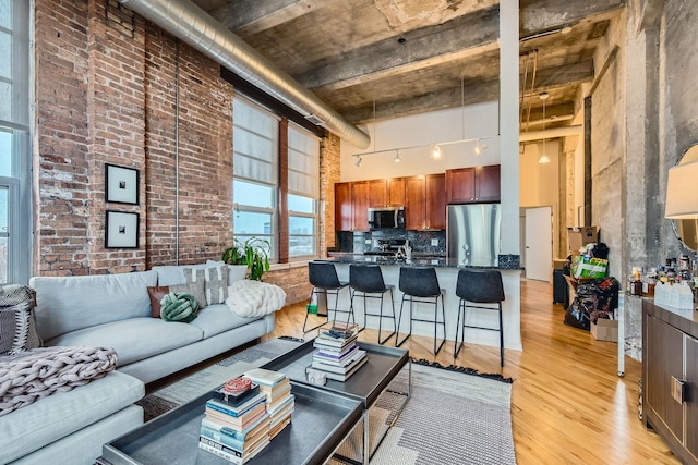 living room featuring a towering ceiling, light wood-style floors, brick wall, and track lighting