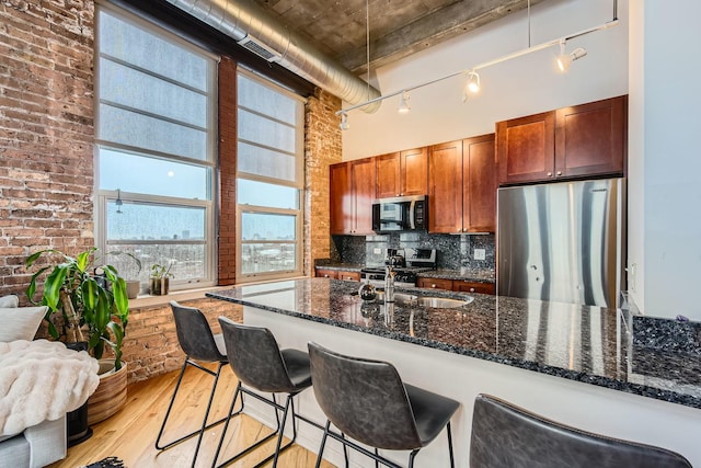 kitchen with backsplash, a high ceiling, appliances with stainless steel finishes, light wood-style floors, and a sink