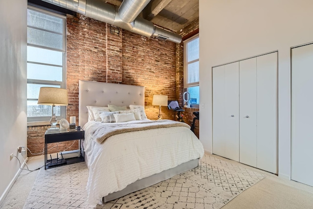 bedroom featuring carpet floors, brick wall, a high ceiling, and two closets