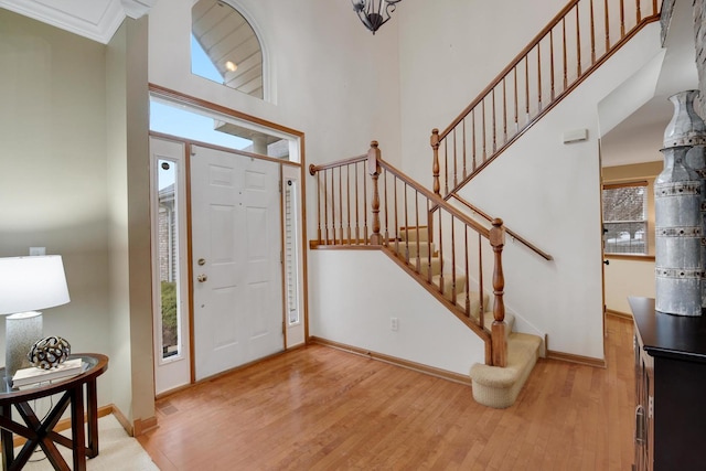 foyer featuring a towering ceiling, light wood-style floors, stairs, and baseboards