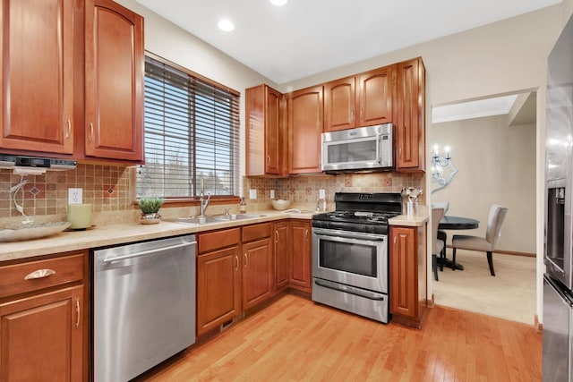 kitchen featuring decorative backsplash, stainless steel appliances, light countertops, light wood-type flooring, and a sink