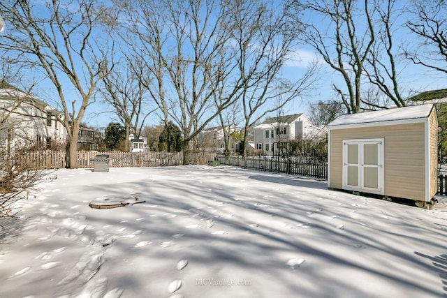 snowy yard featuring a residential view, fence, an outdoor structure, and a storage unit