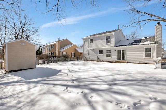 snow covered back of property featuring entry steps, an outbuilding, a storage shed, fence, and a chimney