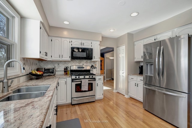 kitchen featuring decorative backsplash, white cabinets, appliances with stainless steel finishes, light stone countertops, and a sink