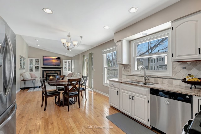 kitchen featuring stainless steel appliances, a brick fireplace, open floor plan, white cabinetry, and a sink