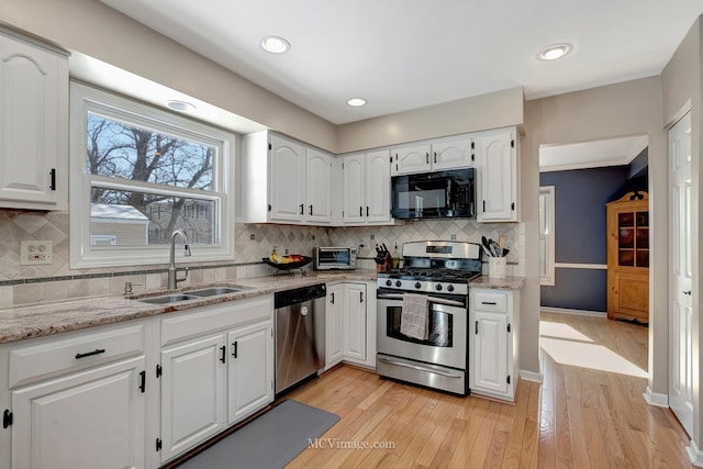 kitchen featuring stainless steel appliances, white cabinetry, a sink, and light stone counters