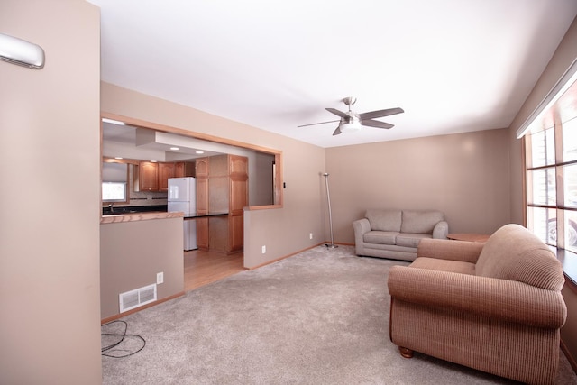 living area featuring ceiling fan, visible vents, baseboards, and light colored carpet