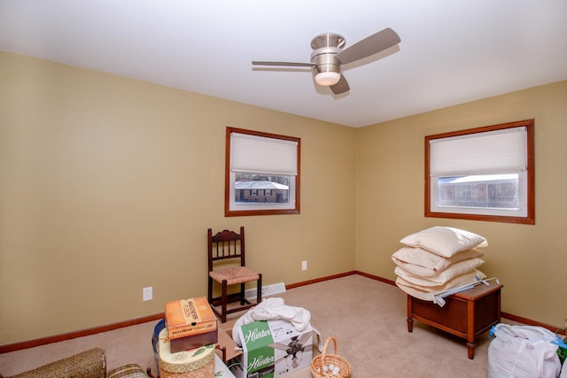 living area featuring baseboards, ceiling fan, and light colored carpet