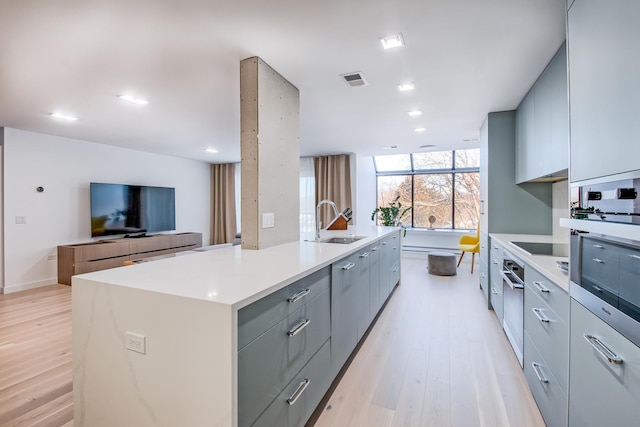 kitchen with light wood finished floors, gray cabinets, light countertops, open floor plan, and a large island with sink