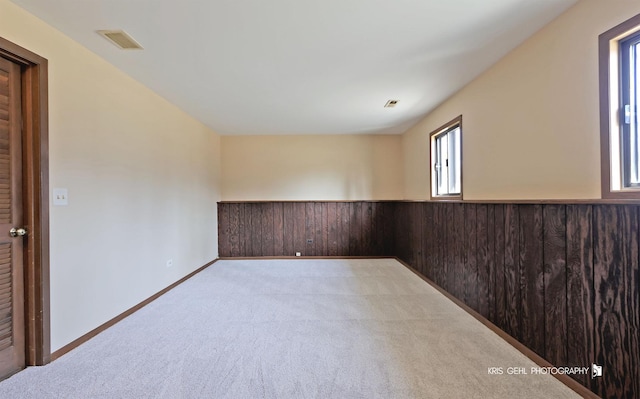 unfurnished room featuring a wainscoted wall, wooden walls, light colored carpet, and visible vents