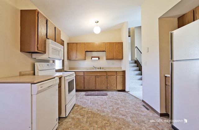 kitchen with white appliances, brown cabinetry, visible vents, a sink, and light countertops