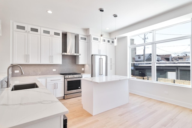 kitchen with glass insert cabinets, wall chimney exhaust hood, appliances with stainless steel finishes, and a sink