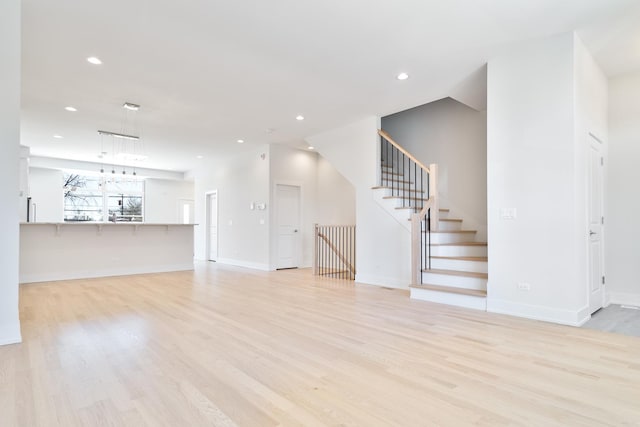 unfurnished living room featuring baseboards, stairway, light wood-style flooring, and recessed lighting