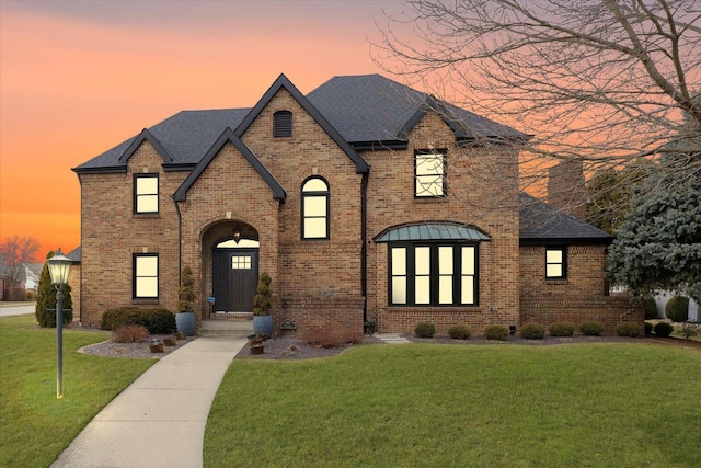 view of front facade with a yard, a shingled roof, and brick siding