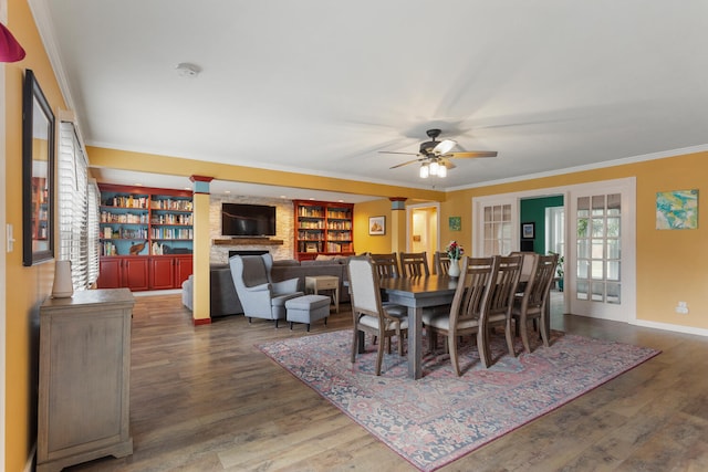 dining room with ornamental molding, ceiling fan, a stone fireplace, and wood finished floors