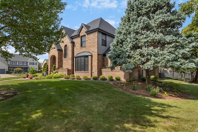 tudor house featuring brick siding, a front yard, and fence