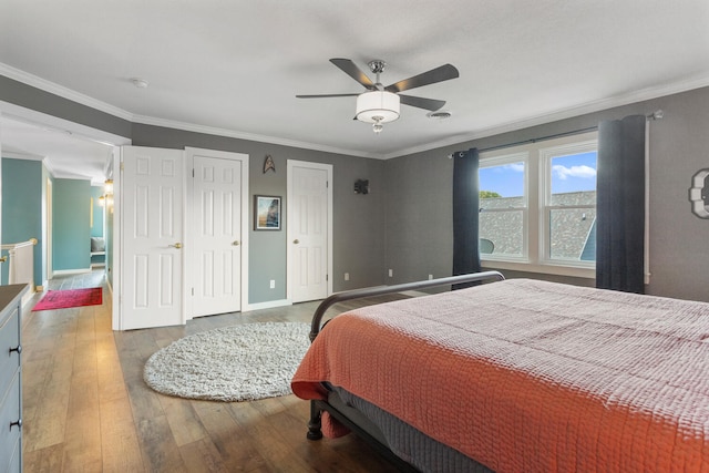 bedroom featuring baseboards, hardwood / wood-style floors, multiple closets, and crown molding