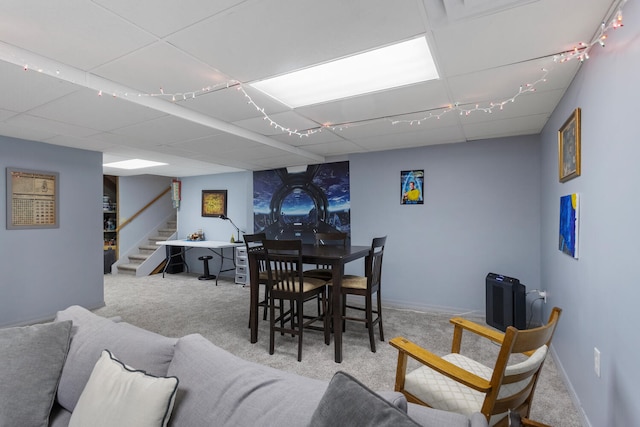 dining area featuring a paneled ceiling, carpet, stairs, and baseboards