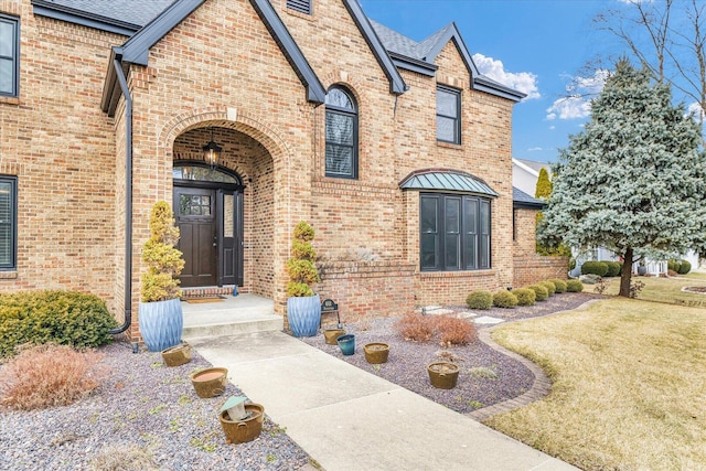 property entrance featuring roof with shingles, brick siding, and a lawn