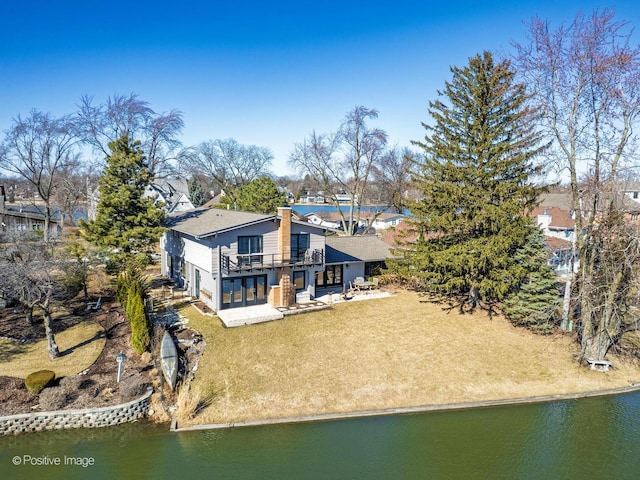 back of house with a patio, a balcony, a chimney, a water view, and a lawn