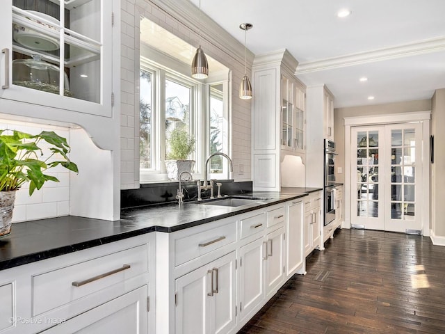 kitchen with dark countertops, glass insert cabinets, dark wood-type flooring, white cabinetry, and a sink