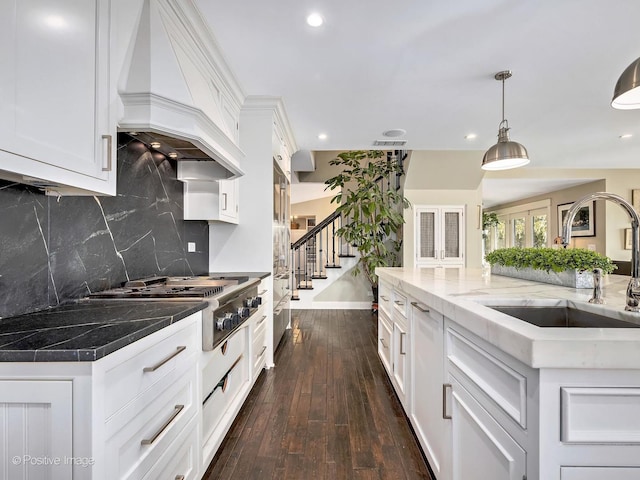 kitchen featuring premium range hood, a sink, white cabinets, backsplash, and dark wood finished floors