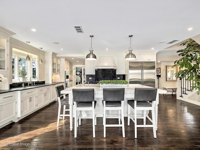 kitchen with custom exhaust hood, visible vents, a sink, and built in fridge