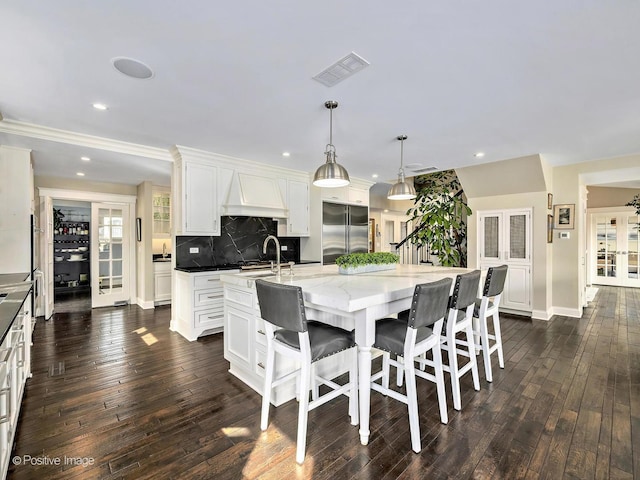 kitchen with a large island, custom exhaust hood, visible vents, stainless steel built in fridge, and a sink