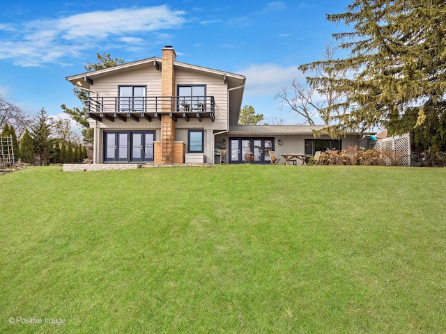 back of house with a chimney, french doors, a lawn, and a balcony