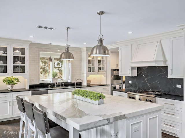 kitchen with visible vents, white cabinets, an island with sink, stove, and premium range hood