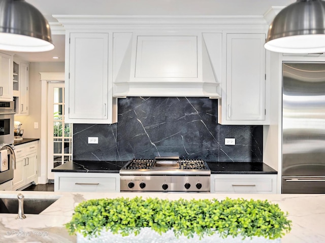 kitchen featuring custom range hood, dark stone countertops, stainless steel appliances, white cabinetry, and backsplash