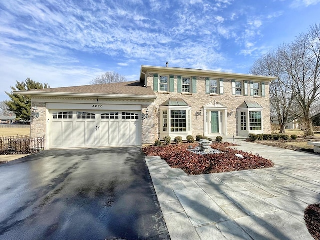 colonial home featuring driveway, brick siding, an attached garage, and fence