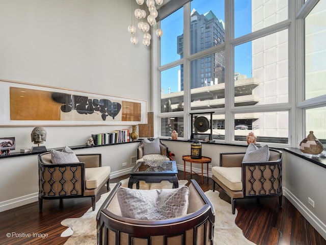 sitting room with a chandelier, wood finished floors, a towering ceiling, and baseboards