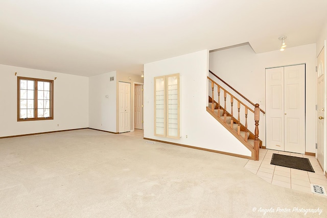 spare room featuring light carpet, stairs, and baseboards