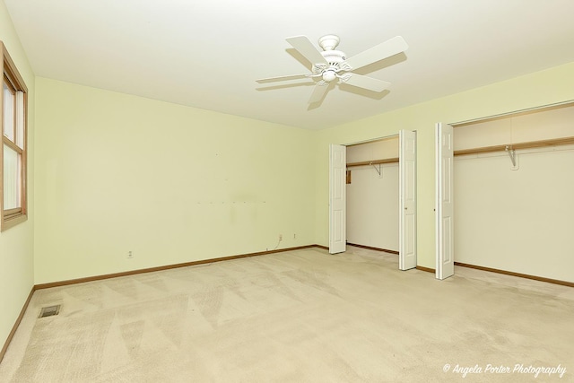 unfurnished bedroom with light colored carpet, visible vents, multiple closets, and baseboards