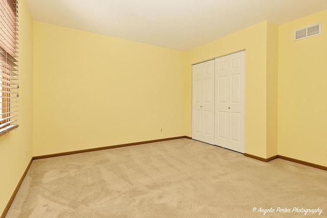 unfurnished bedroom featuring a closet, visible vents, light colored carpet, and baseboards