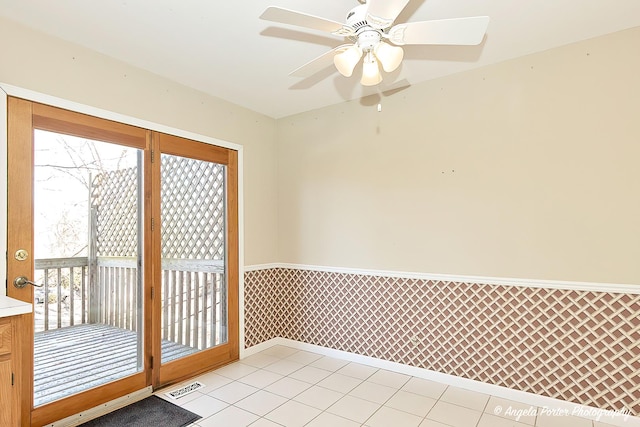 doorway featuring light tile patterned floors, visible vents, a ceiling fan, and wainscoting