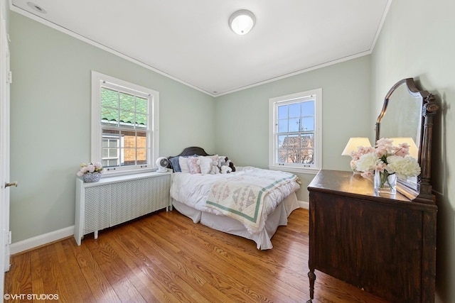 bedroom with multiple windows, crown molding, light wood-style flooring, and radiator heating unit